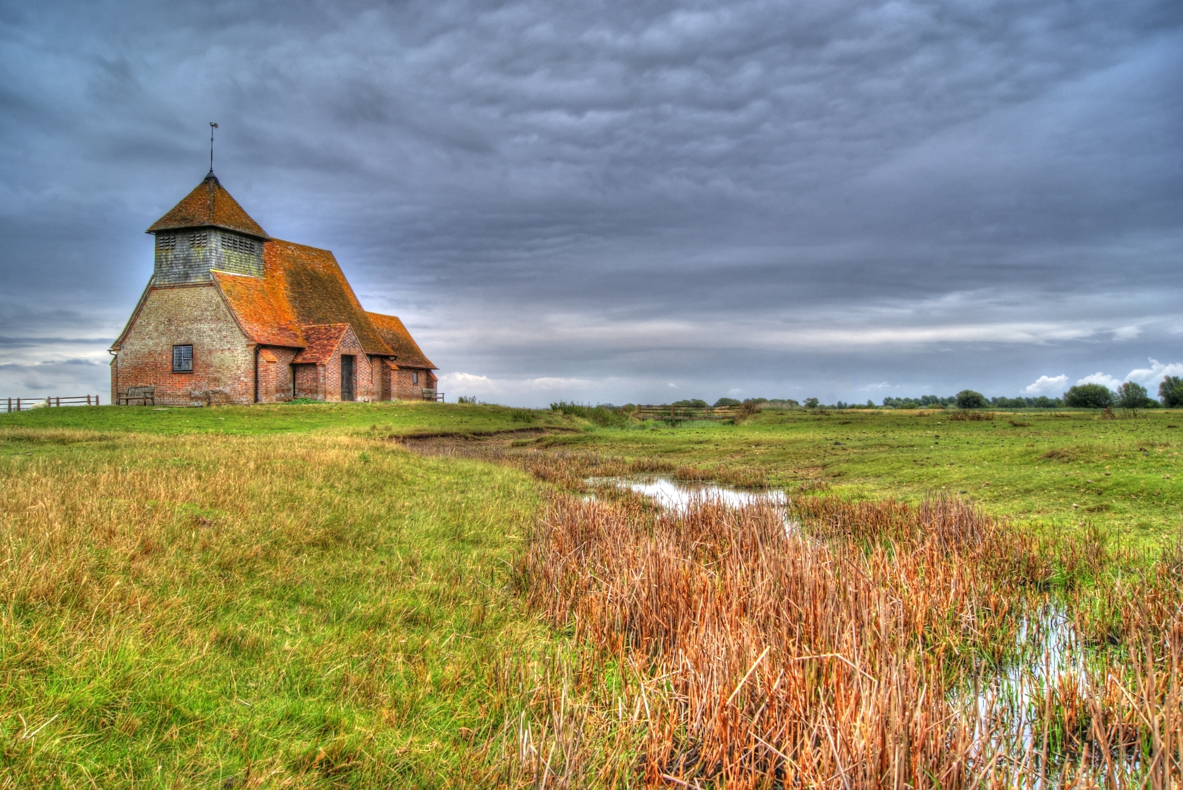 St Thomas Becket Church standing on Romney Marsh beneath a dramatic sky